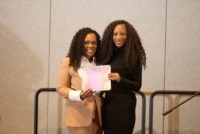 Two women smiling, holding a certificate together.